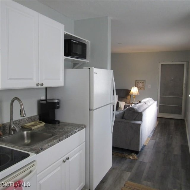 kitchen with dark wood-type flooring, freestanding refrigerator, white cabinetry, a sink, and black microwave