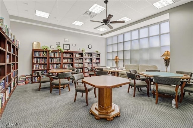 interior space featuring ceiling fan, a drop ceiling, a towering ceiling, visible vents, and wall of books