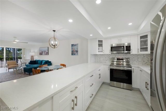 kitchen with kitchen peninsula, white cabinets, backsplash, appliances with stainless steel finishes, and light hardwood / wood-style flooring