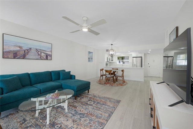 living room with ceiling fan with notable chandelier, plenty of natural light, and light wood-style floors