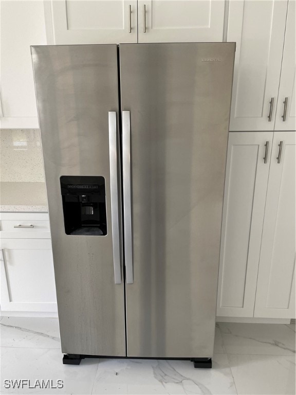 details featuring stainless steel fridge, light stone countertops, and white cabinets