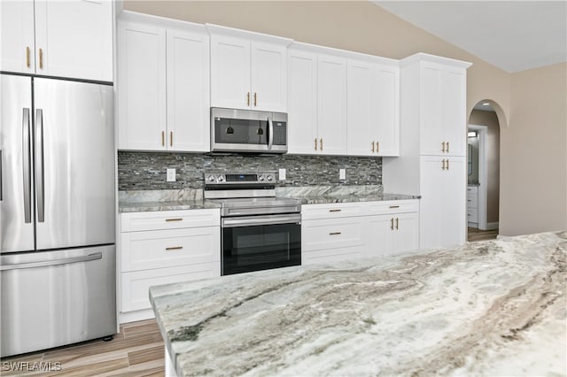 kitchen with white cabinetry, appliances with stainless steel finishes, vaulted ceiling, and decorative backsplash