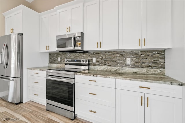 kitchen with tasteful backsplash, appliances with stainless steel finishes, white cabinetry, light stone counters, and light hardwood / wood-style flooring