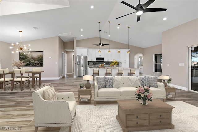 living room featuring light hardwood / wood-style flooring, ceiling fan with notable chandelier, and vaulted ceiling