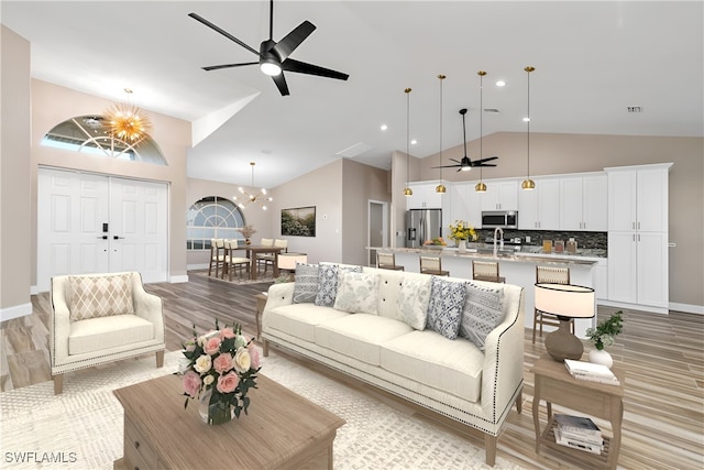 living room featuring light hardwood / wood-style floors, high vaulted ceiling, sink, and ceiling fan with notable chandelier