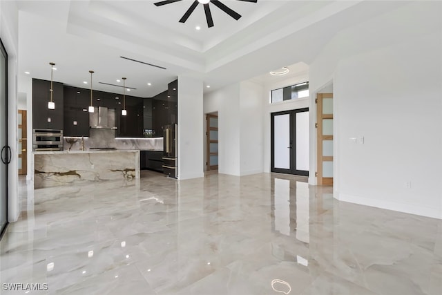 interior space with hanging light fixtures, wall chimney exhaust hood, appliances with stainless steel finishes, a tray ceiling, and a center island