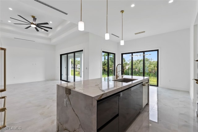 kitchen with light stone counters, an island with sink, dark brown cabinets, decorative light fixtures, and sink