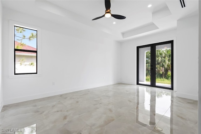 empty room featuring a healthy amount of sunlight, a tray ceiling, and ceiling fan