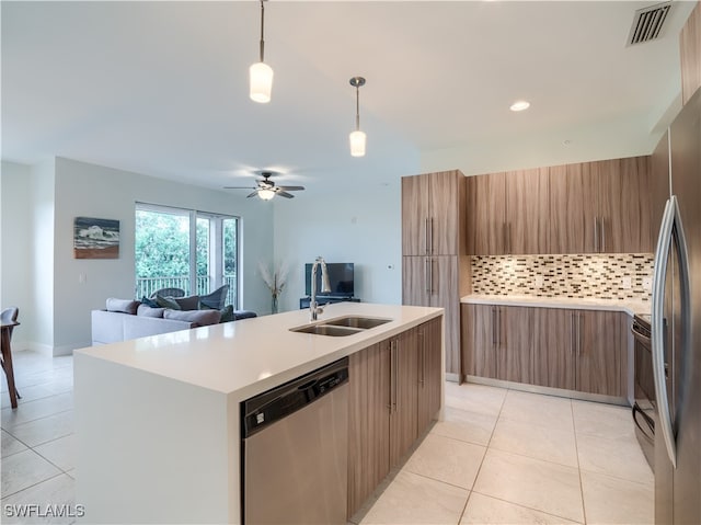 kitchen with hanging light fixtures, decorative backsplash, an island with sink, stainless steel appliances, and ceiling fan