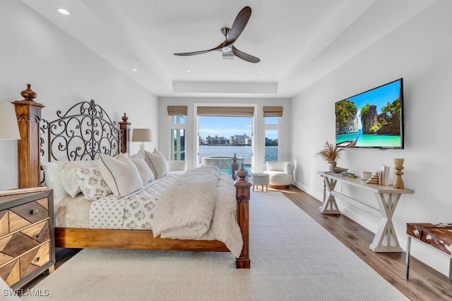 bedroom with ceiling fan, hardwood / wood-style flooring, a raised ceiling, and access to outside