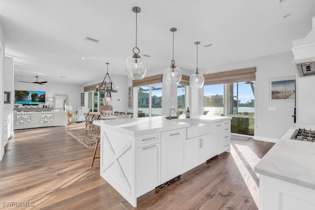 kitchen with hanging light fixtures, ceiling fan, white cabinetry, and a center island with sink