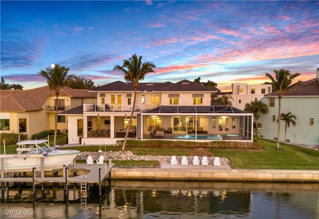 back house at dusk with a water view, a balcony, a yard, and a lanai