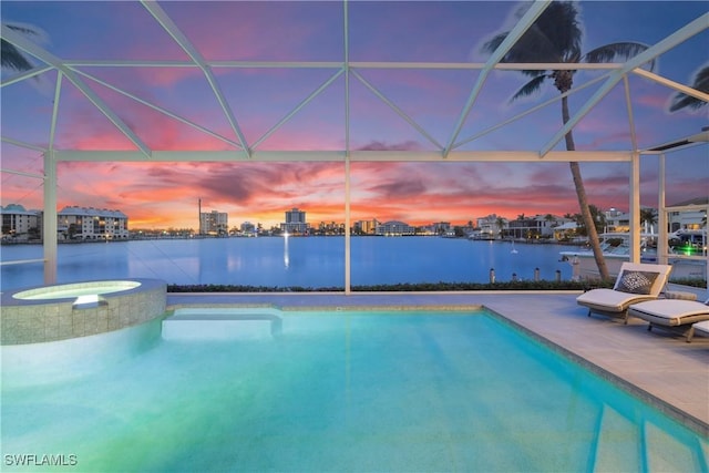 pool at dusk with an in ground hot tub, a patio area, glass enclosure, and a water view