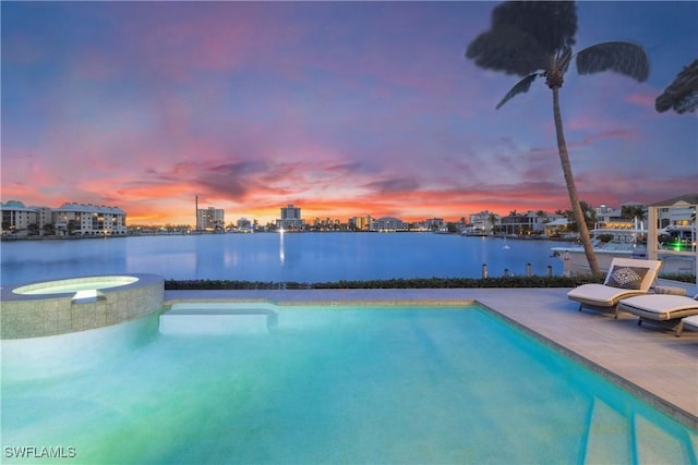 pool at dusk featuring a water view, a patio area, and an in ground hot tub