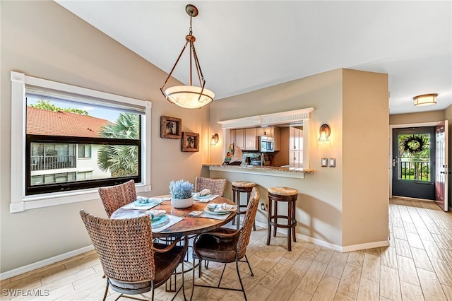 dining room with light wood-style flooring, vaulted ceiling, and baseboards