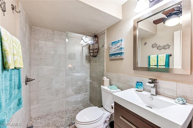 bathroom with a tile shower, toilet, vanity, tile walls, and a textured ceiling