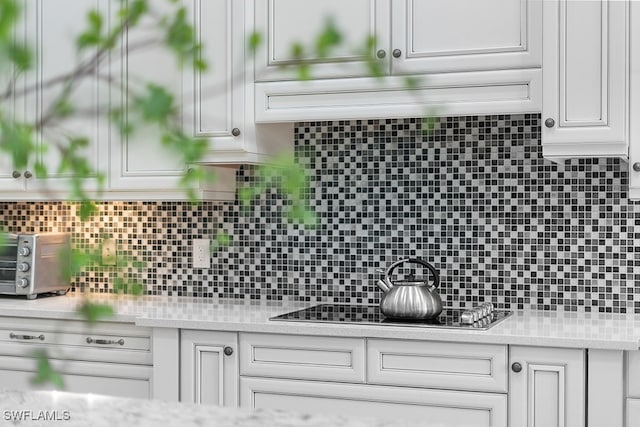 kitchen featuring black stovetop, light stone countertops, white cabinetry, and decorative backsplash