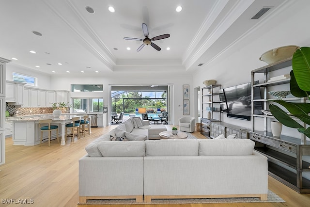 living room featuring light hardwood / wood-style floors, ceiling fan, a tray ceiling, and crown molding