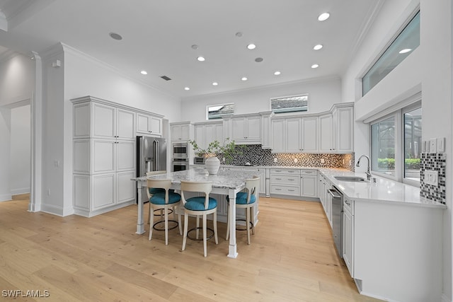 kitchen with a kitchen island, a kitchen bar, light hardwood / wood-style flooring, ornamental molding, and sink