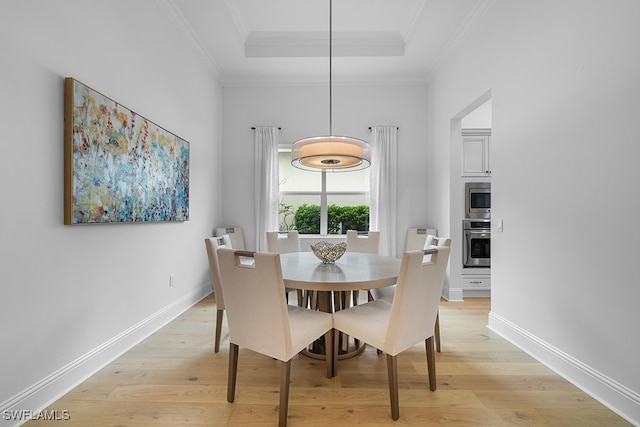 dining space featuring light wood-type flooring, a raised ceiling, and ornamental molding