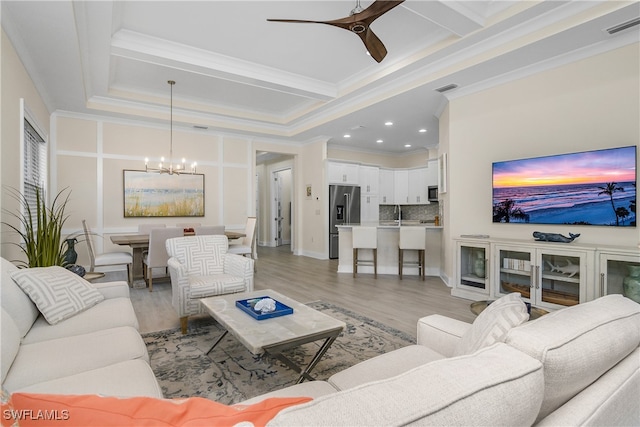 living room featuring a raised ceiling, light hardwood / wood-style flooring, coffered ceiling, ceiling fan with notable chandelier, and crown molding