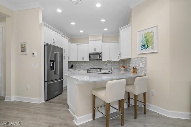 kitchen featuring appliances with stainless steel finishes, white cabinetry, tasteful backsplash, a kitchen bar, and light hardwood / wood-style flooring