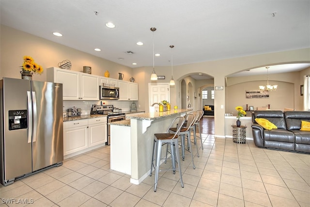 kitchen with appliances with stainless steel finishes, stone counters, pendant lighting, and white cabinets