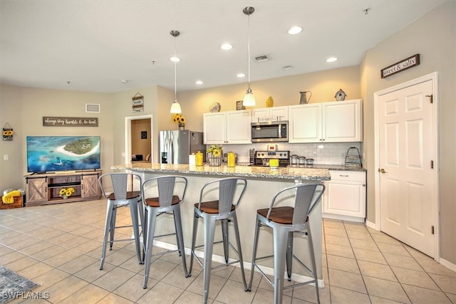 kitchen with light stone counters, a center island with sink, white cabinetry, stainless steel appliances, and a kitchen bar