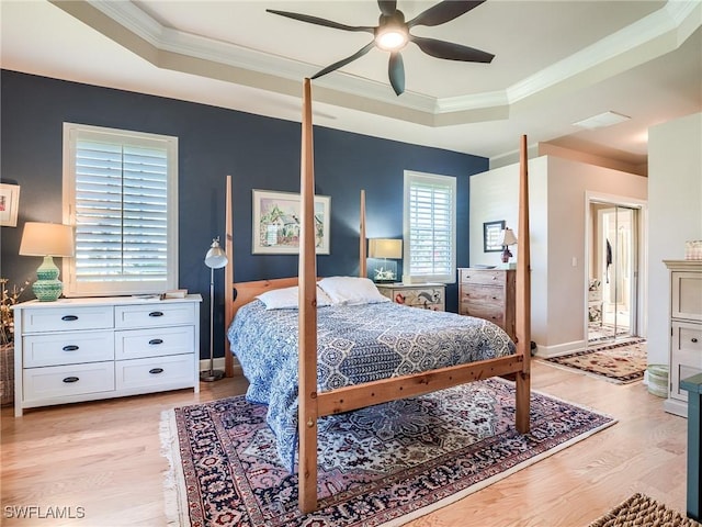 bedroom with crown molding, light hardwood / wood-style floors, a raised ceiling, and ceiling fan