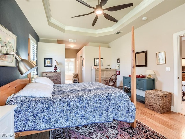 bedroom with ceiling fan, a tray ceiling, multiple windows, and light hardwood / wood-style flooring