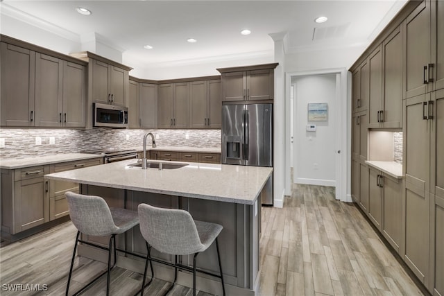 kitchen featuring sink, a center island with sink, light hardwood / wood-style flooring, stainless steel appliances, and crown molding