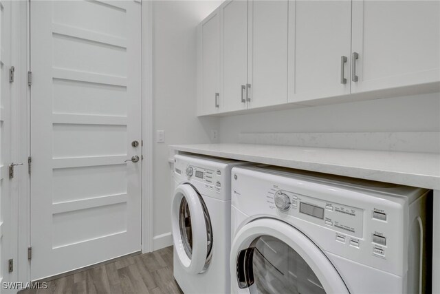 laundry area featuring light hardwood / wood-style floors, washing machine and clothes dryer, and cabinets