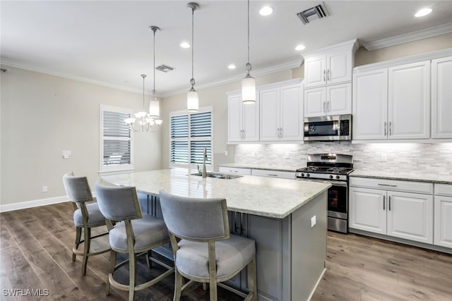 kitchen with white cabinets, sink, a kitchen island with sink, appliances with stainless steel finishes, and an inviting chandelier