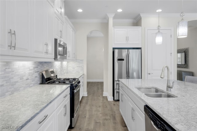 kitchen with appliances with stainless steel finishes, hanging light fixtures, white cabinetry, light wood-type flooring, and sink