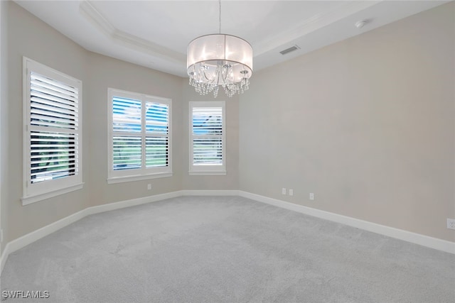 carpeted spare room with a raised ceiling, ornamental molding, and a notable chandelier