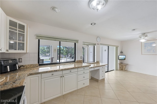 kitchen featuring light tile patterned floors, black range, white cabinetry, light stone countertops, and decorative backsplash