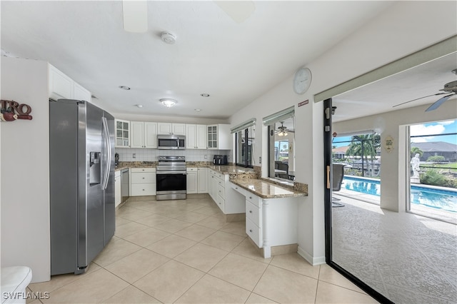 kitchen with light stone counters, white cabinets, backsplash, appliances with stainless steel finishes, and light tile patterned floors