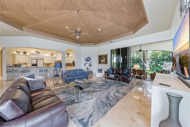 living room featuring a high ceiling, wood ceiling, ceiling fan, and a raised ceiling