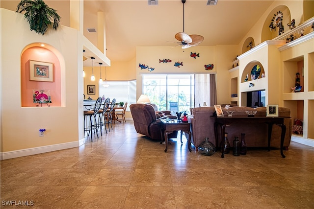 living room with built in shelves, ceiling fan, and a high ceiling