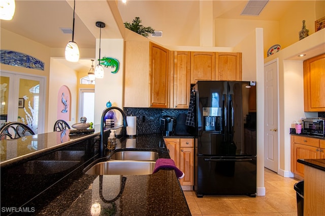 kitchen featuring sink, hanging light fixtures, tasteful backsplash, dark stone counters, and black fridge with ice dispenser