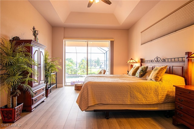 bedroom featuring access to exterior, light hardwood / wood-style floors, a raised ceiling, and ceiling fan