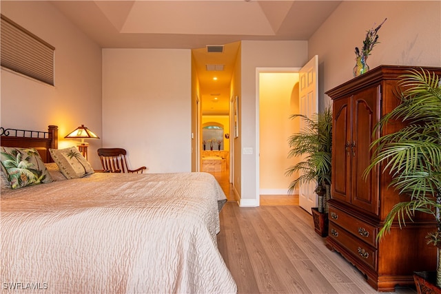 bedroom featuring a tray ceiling, ensuite bath, and light hardwood / wood-style floors