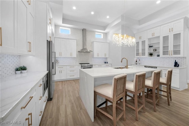 kitchen with tasteful backsplash, sink, white cabinets, and wall chimney range hood