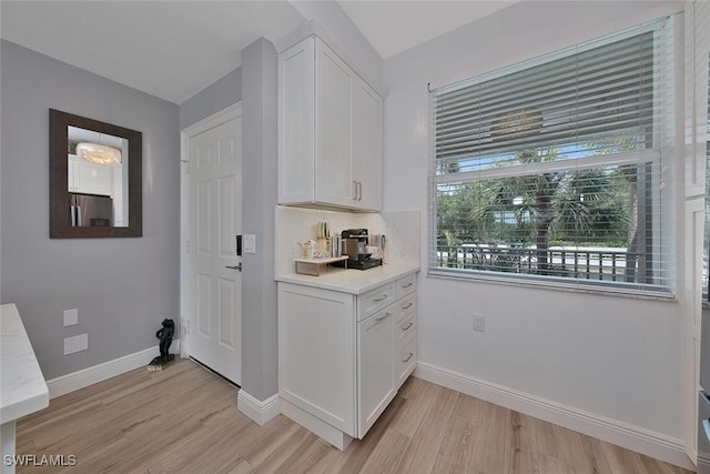 kitchen with white cabinets, stainless steel fridge, light wood-type flooring, and backsplash