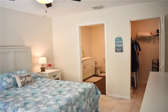 tiled bedroom featuring a closet, ensuite bath, ceiling fan, and a walk in closet