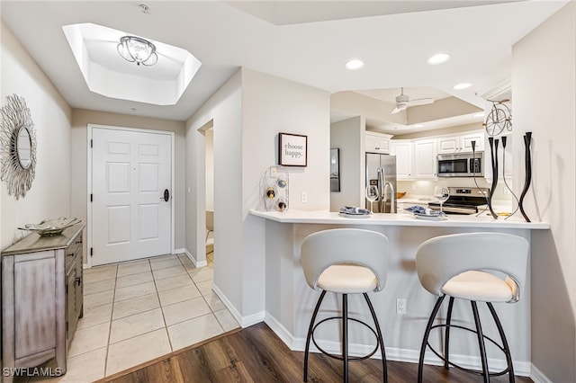 kitchen with white cabinets, a kitchen breakfast bar, light hardwood / wood-style floors, kitchen peninsula, and stainless steel appliances