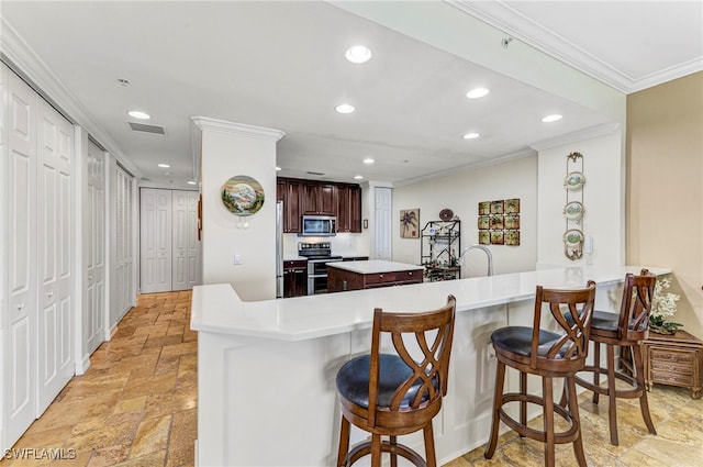 kitchen featuring kitchen peninsula, ornamental molding, a kitchen bar, and stainless steel appliances