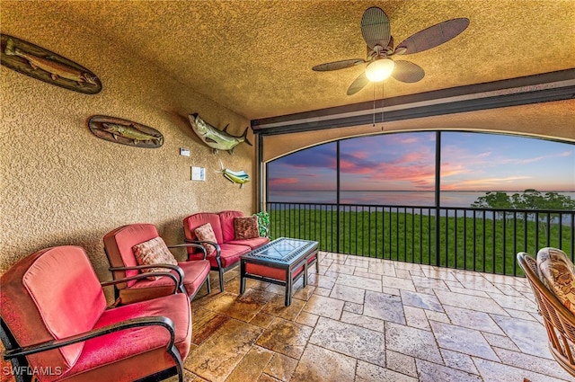 patio terrace at dusk with ceiling fan, an outdoor hangout area, and a lawn