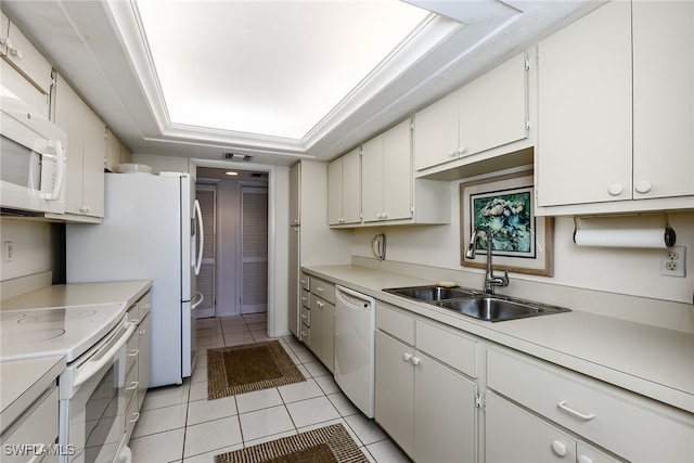 kitchen with a raised ceiling, light tile patterned floors, sink, white appliances, and white cabinetry