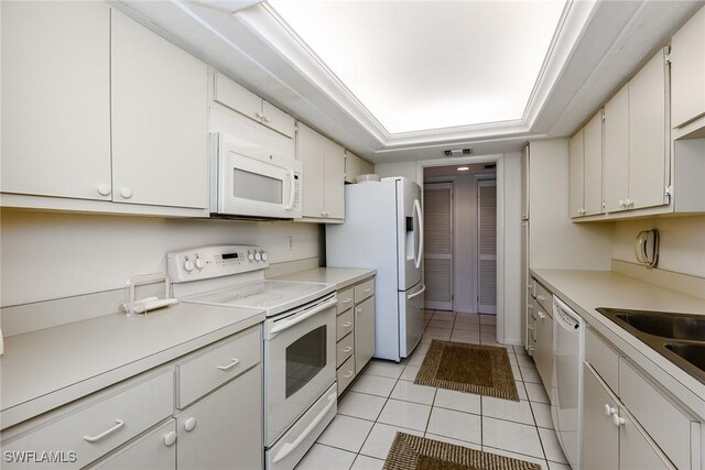 kitchen featuring white cabinets, white appliances, a tray ceiling, and light tile patterned floors